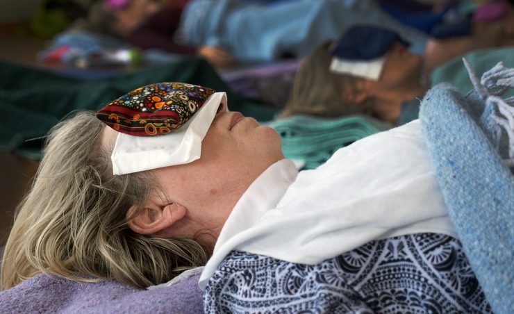 Woman laying on her back with an eye pillow over her eyes receiving guided meditation Yoga Nidra