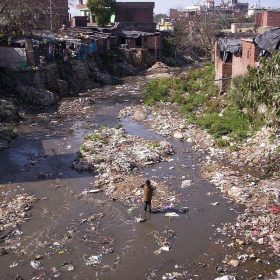 Trash-laden river and a boy standing in the middle in India